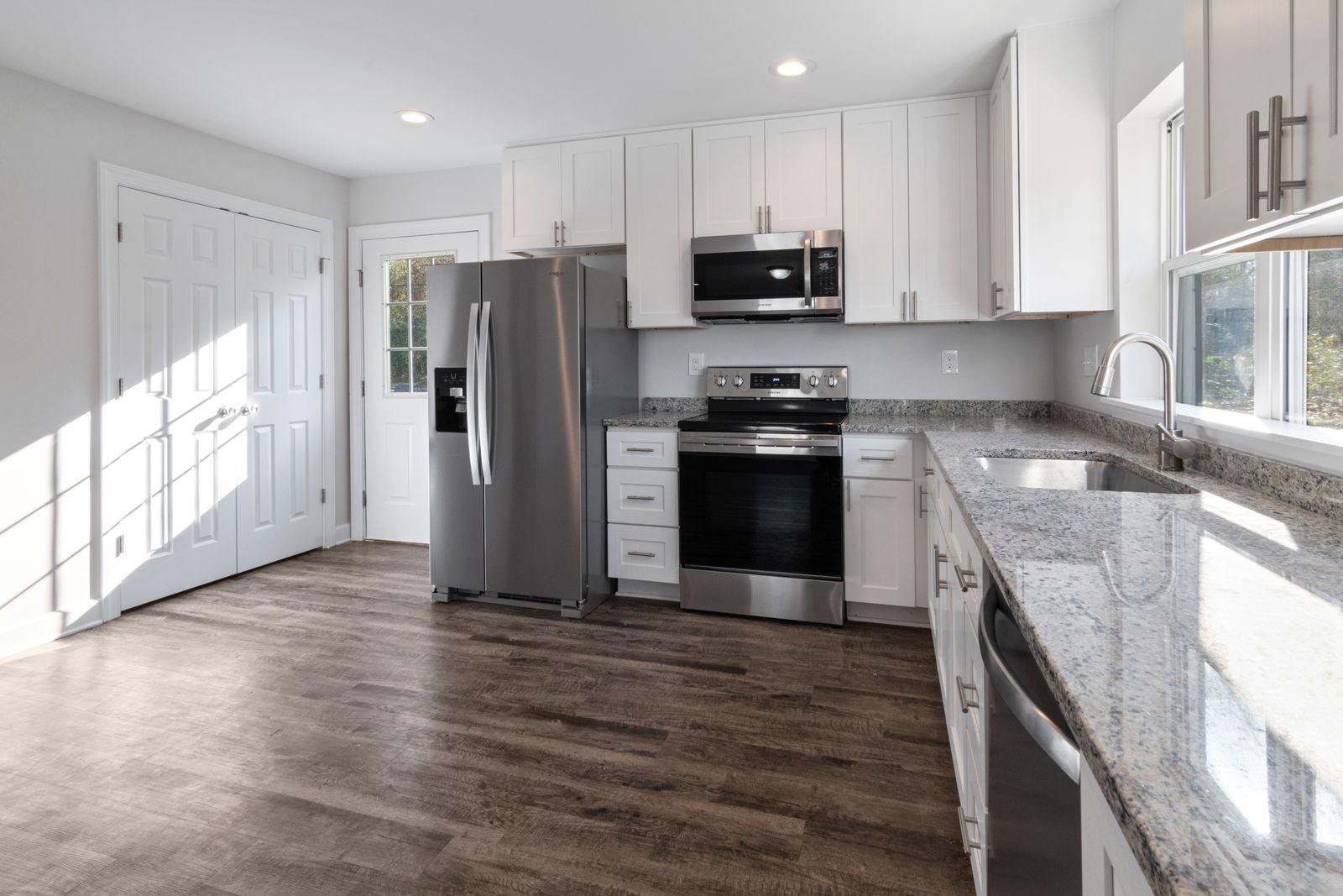 Open-plan L-shaped kitchen in white oak with a dark stone counter